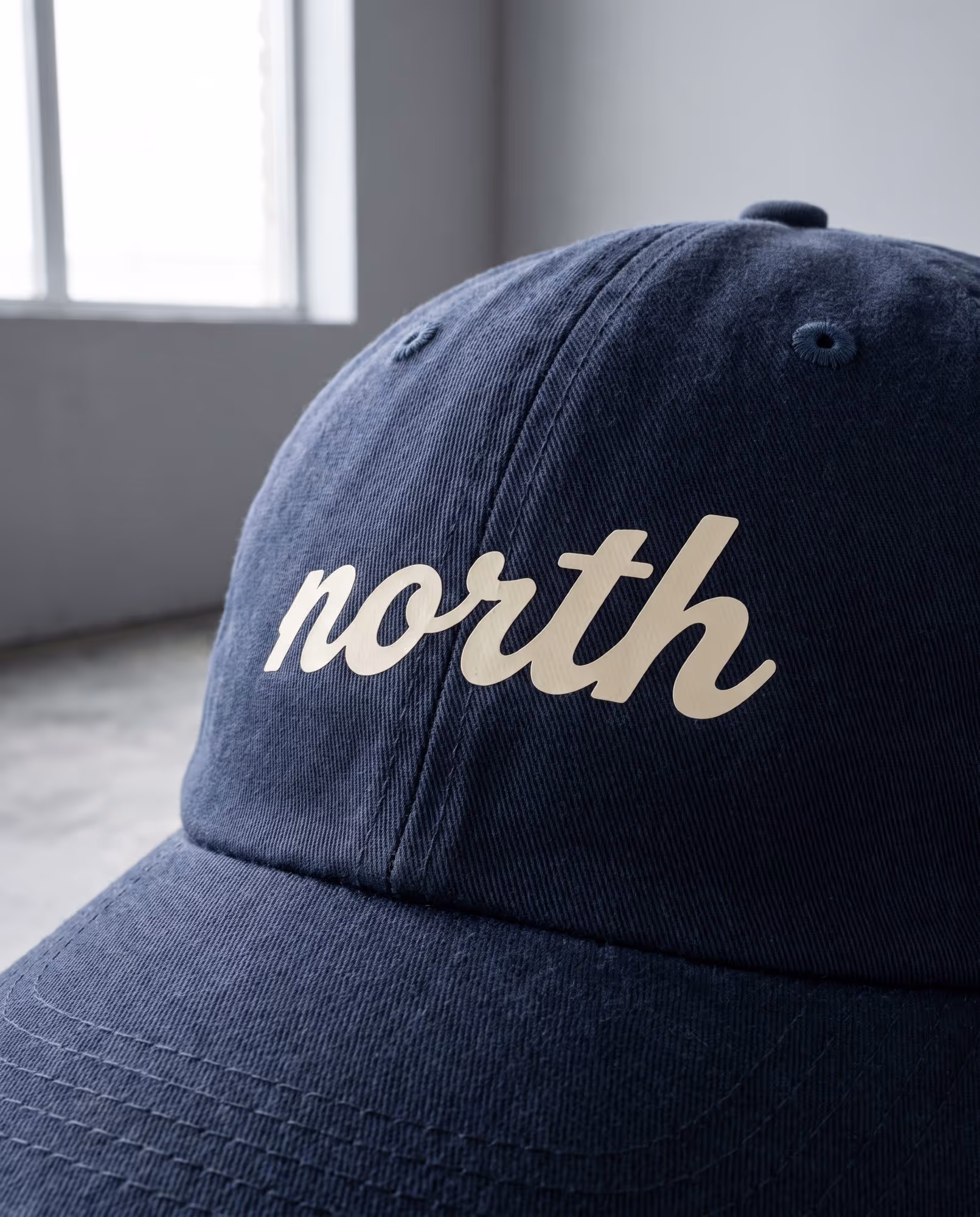 Close-up of cream script lettering printed flat on the front panel of a navy cap