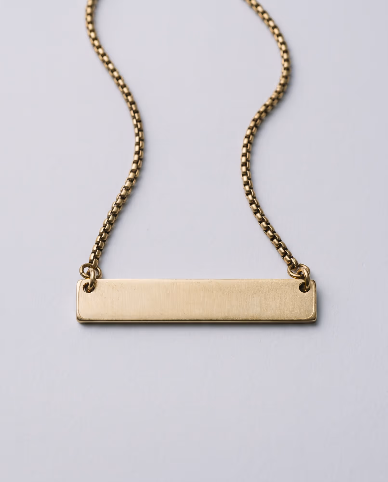 Blank gold-tone bar pendant with a brushed finish on an antique gold-tone box chain