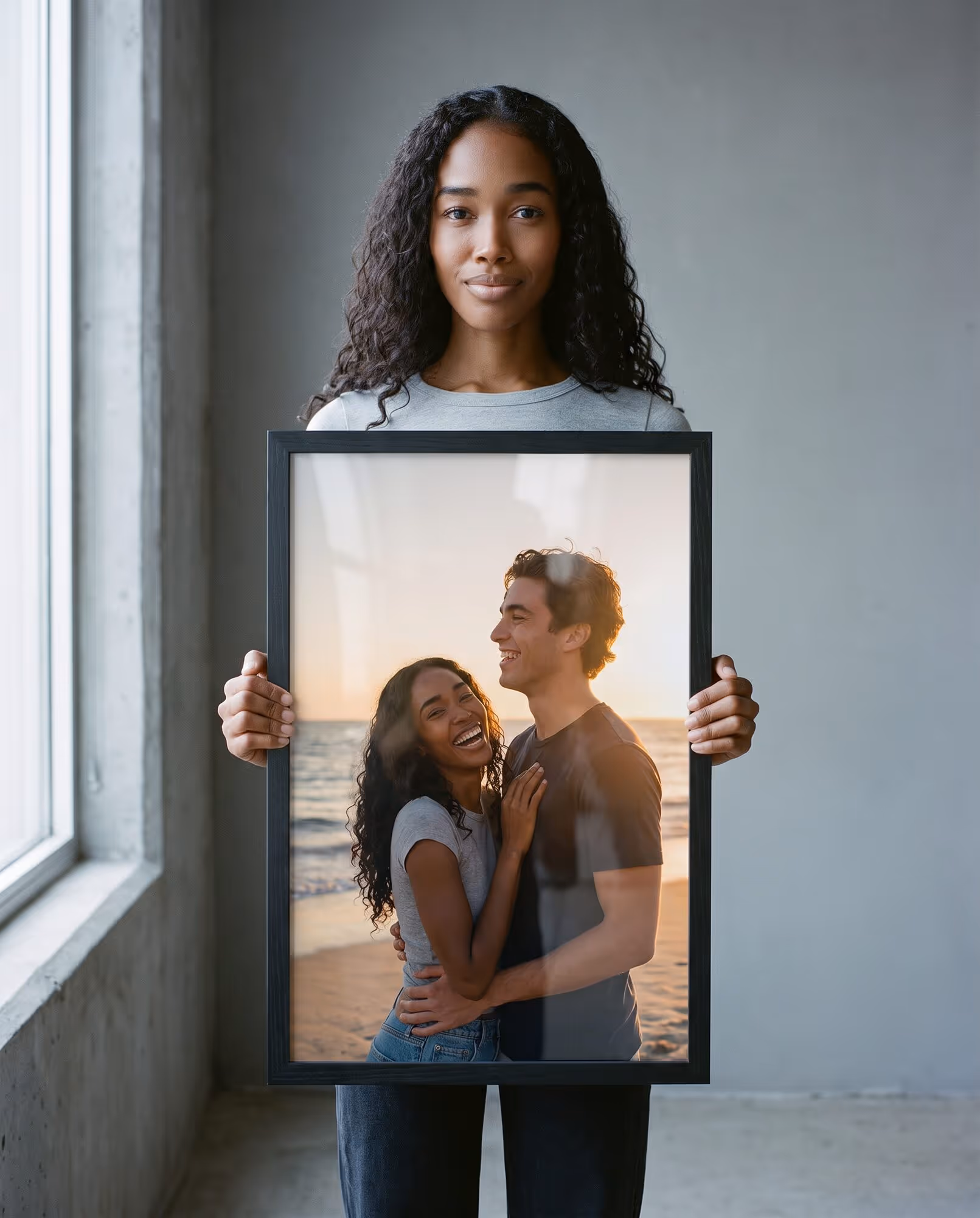 Woman holding up a black wooden 11 by 17 inch portrait frame with a printed beach photo of a laughing couple at sunset