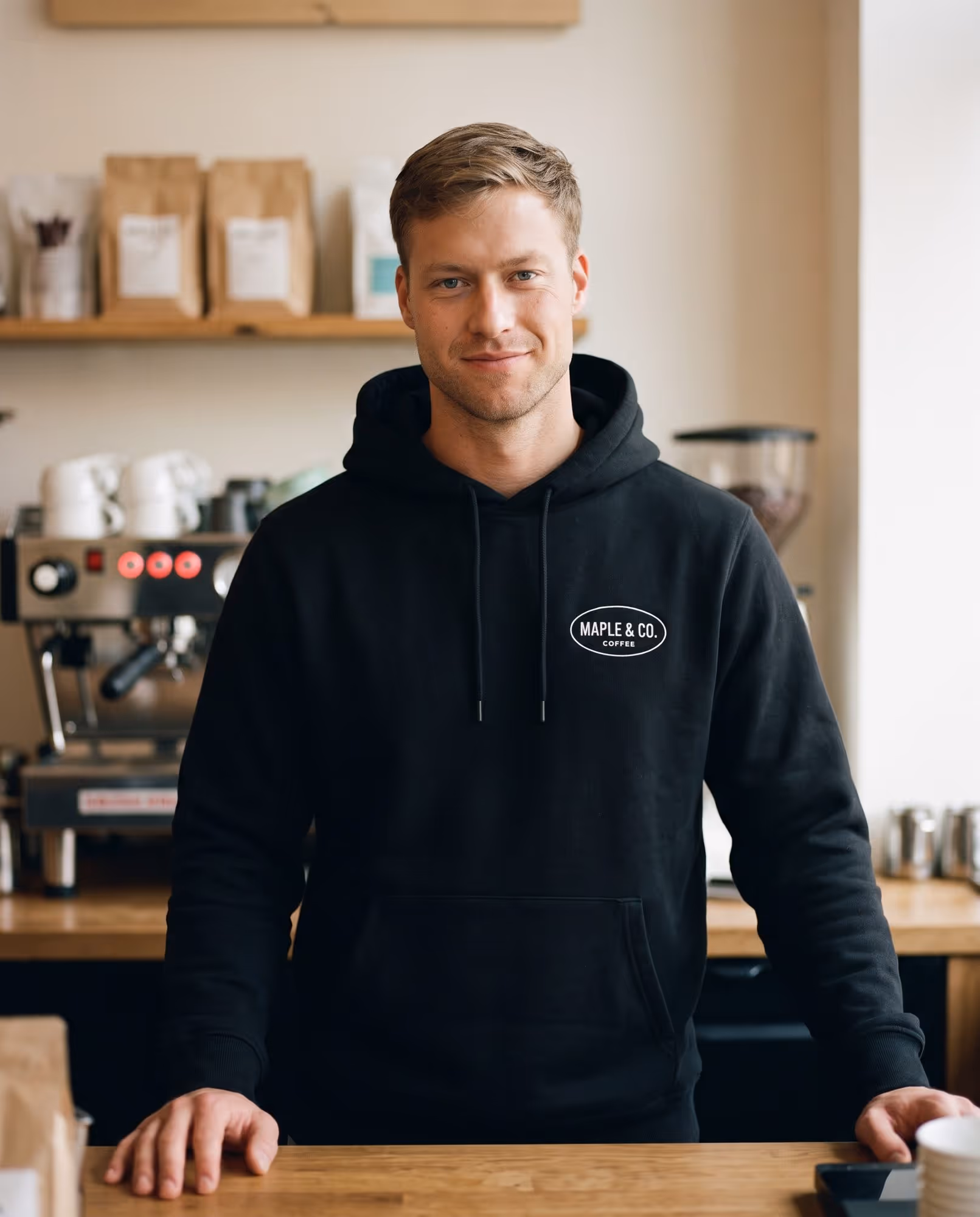 Café staff member in a black hoodie with a small printed oval logo on the chest