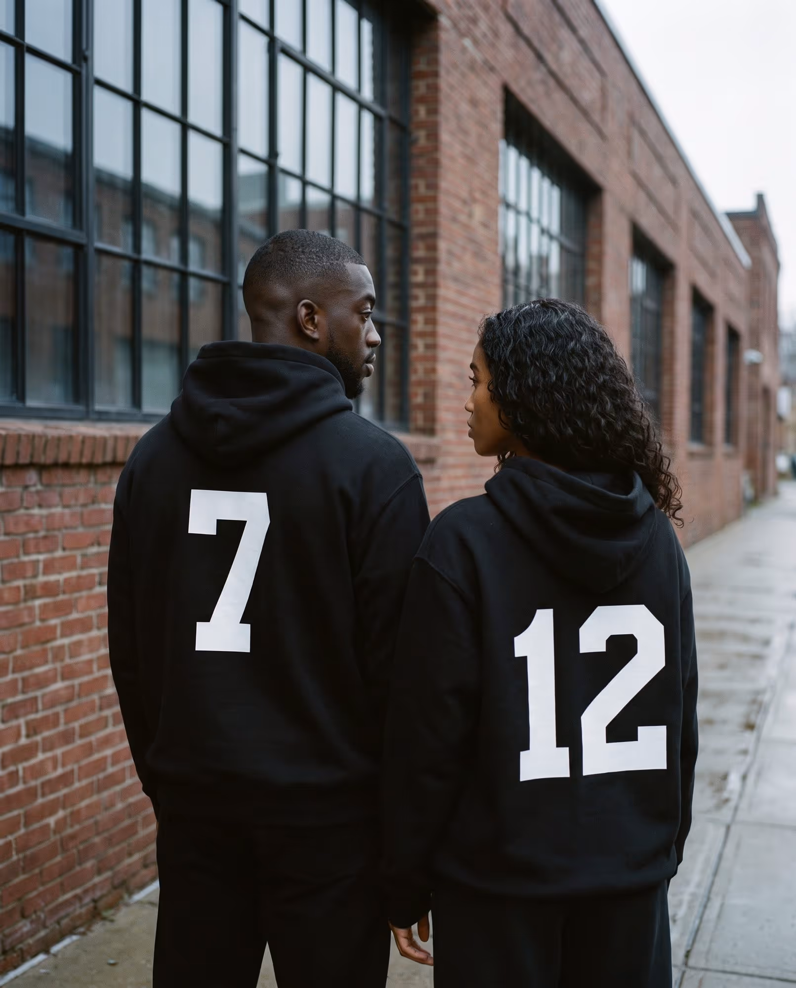 Two people in matching black hoodies with large white numbers printed on the back
