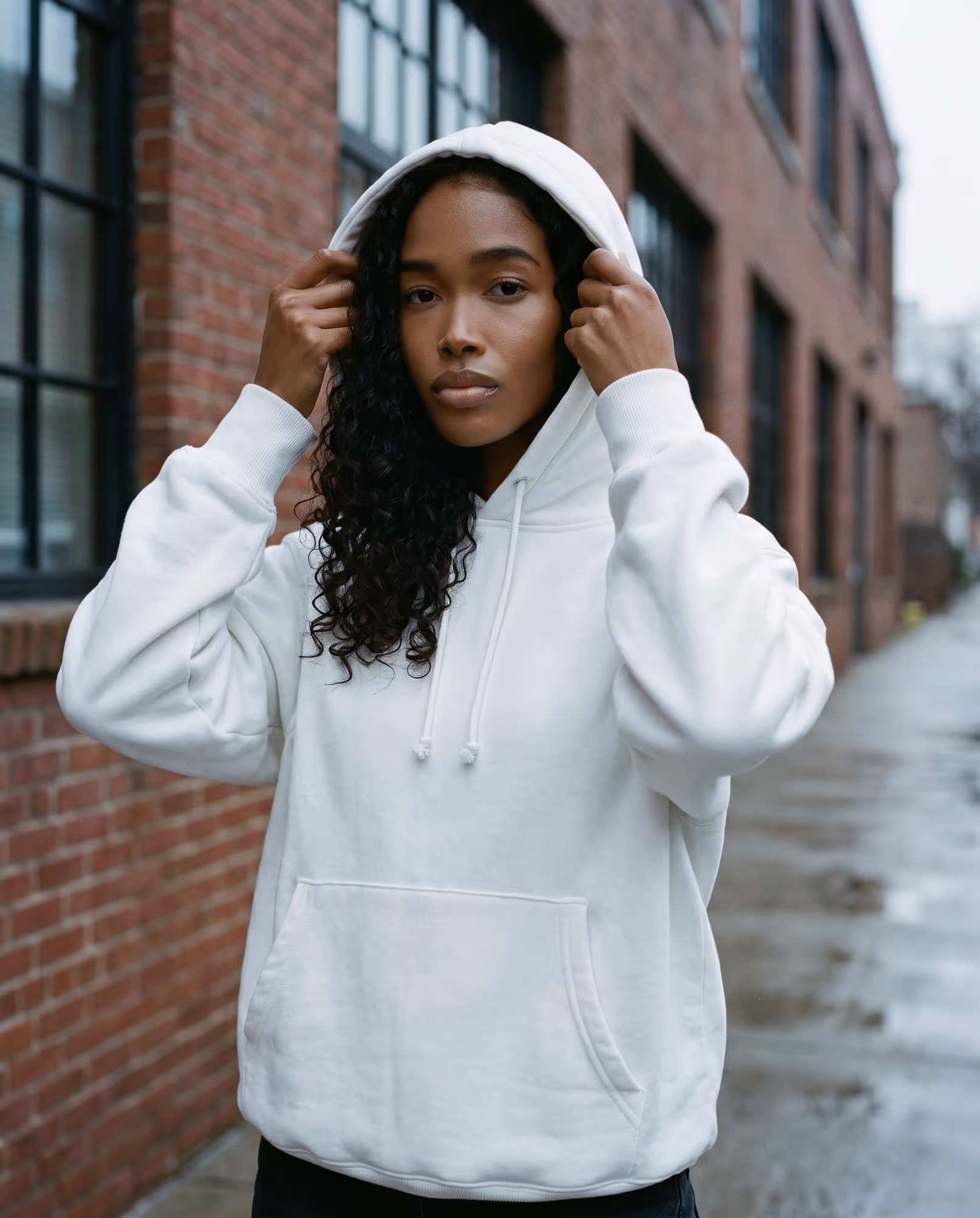 Model pulling up the hood of the plain white pullover hoodie blank