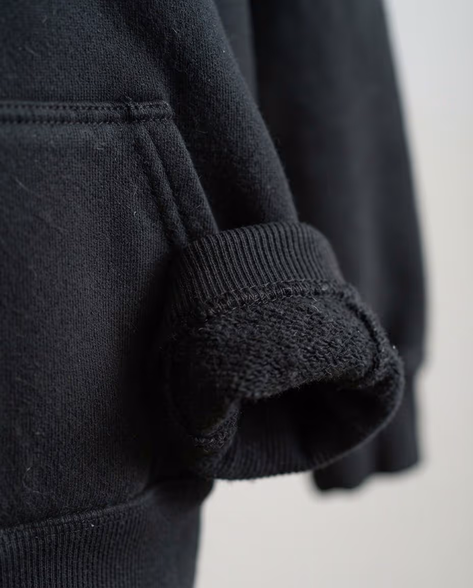 Close-up of the ribbed cuff and kangaroo pocket on a black pullover hoodie