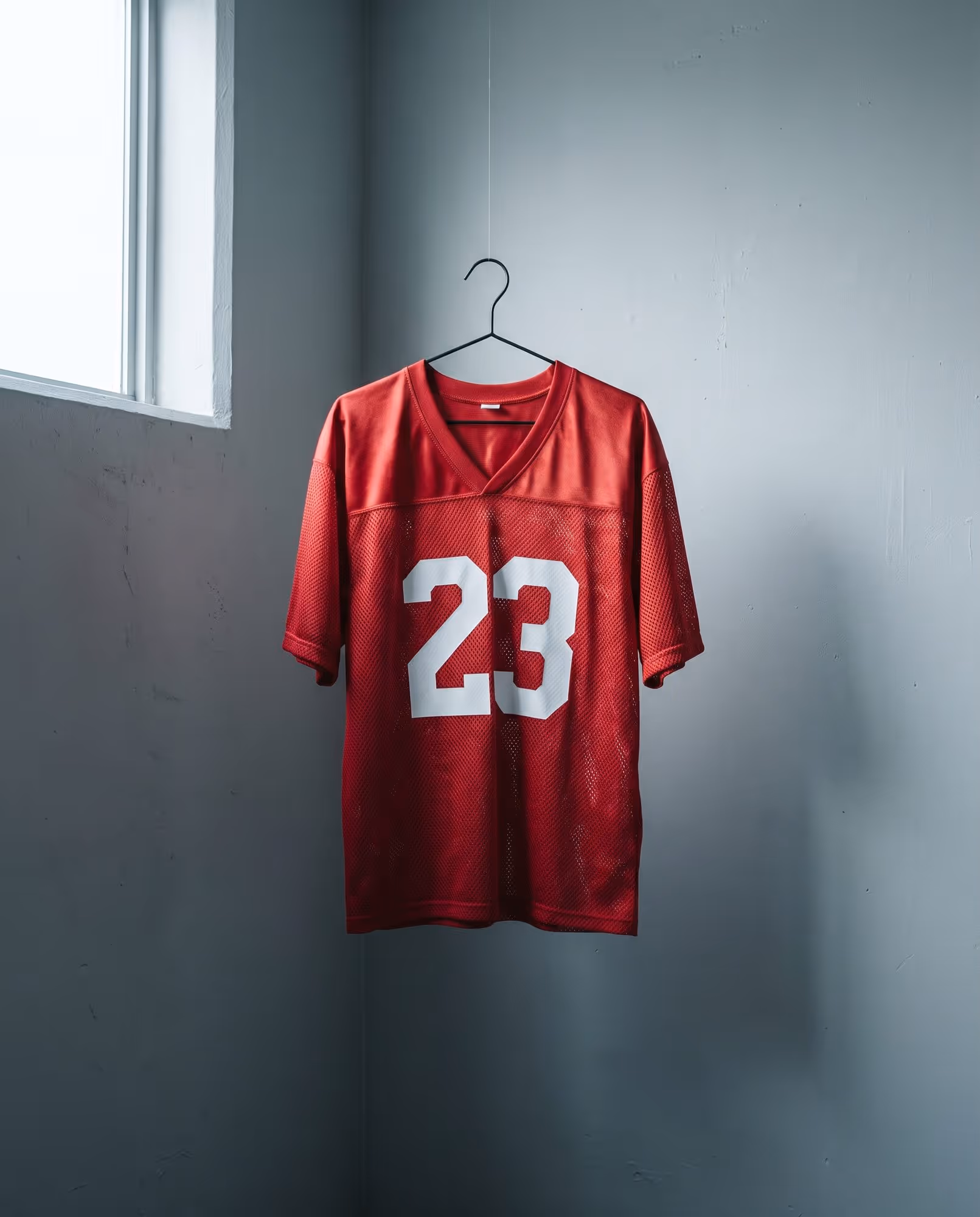 Red mesh football jersey with a white number 23 hanging on a wire hanger