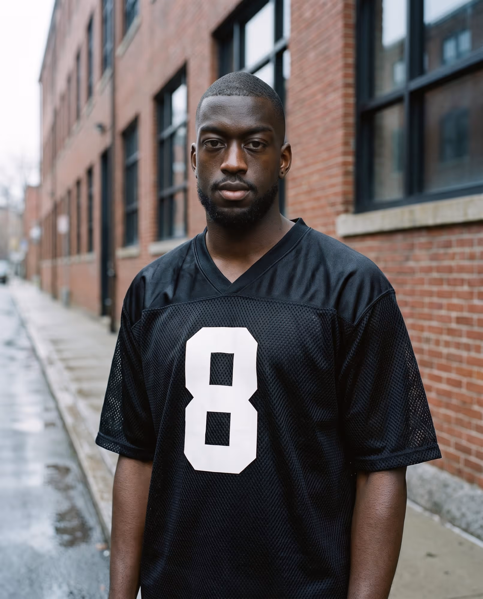 Model in a black mesh football jersey with a white heat-pressed number 8, photographed on a Cambridge street