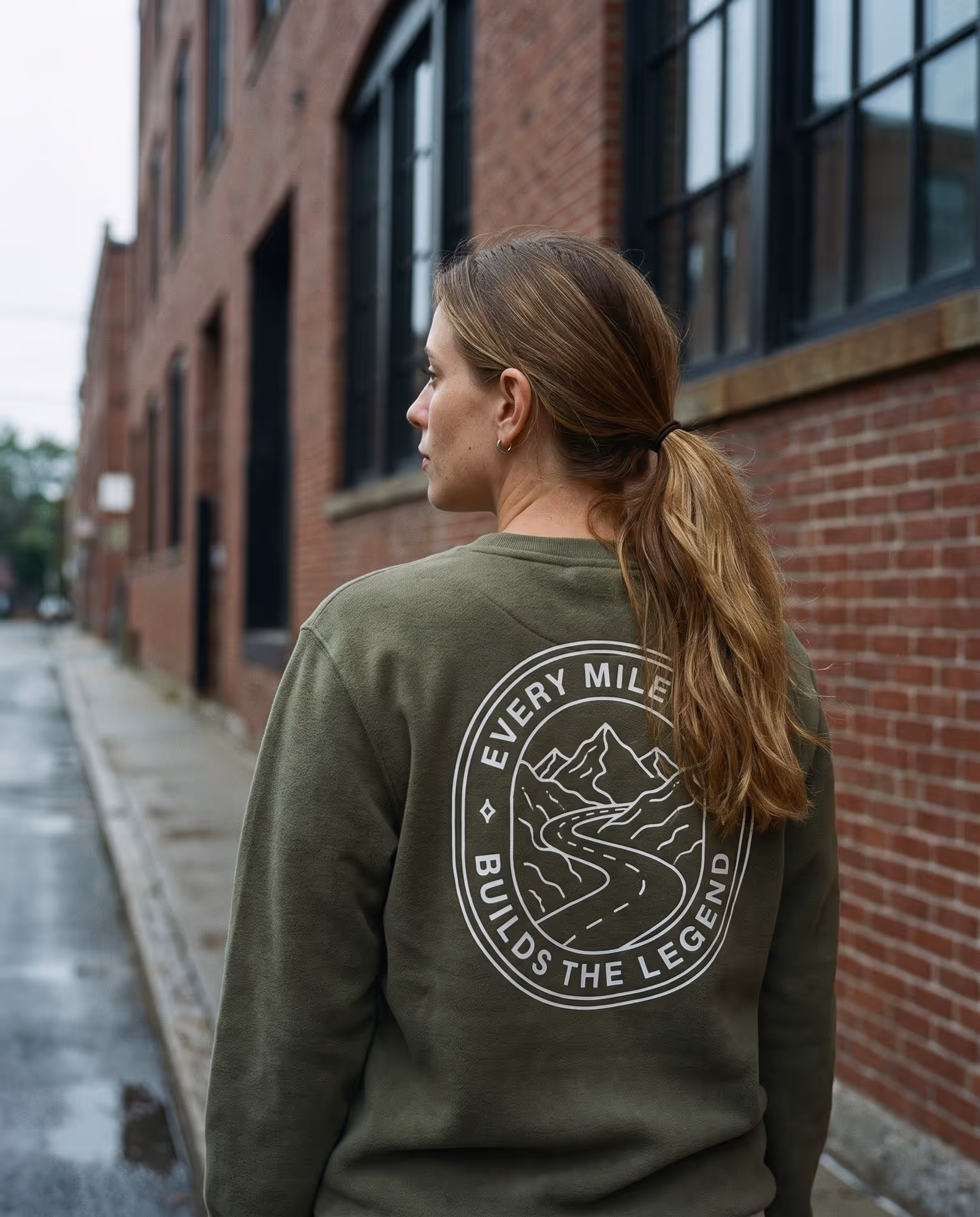Olive crewneck sweatshirt with a white printed mile-badge graphic across the back