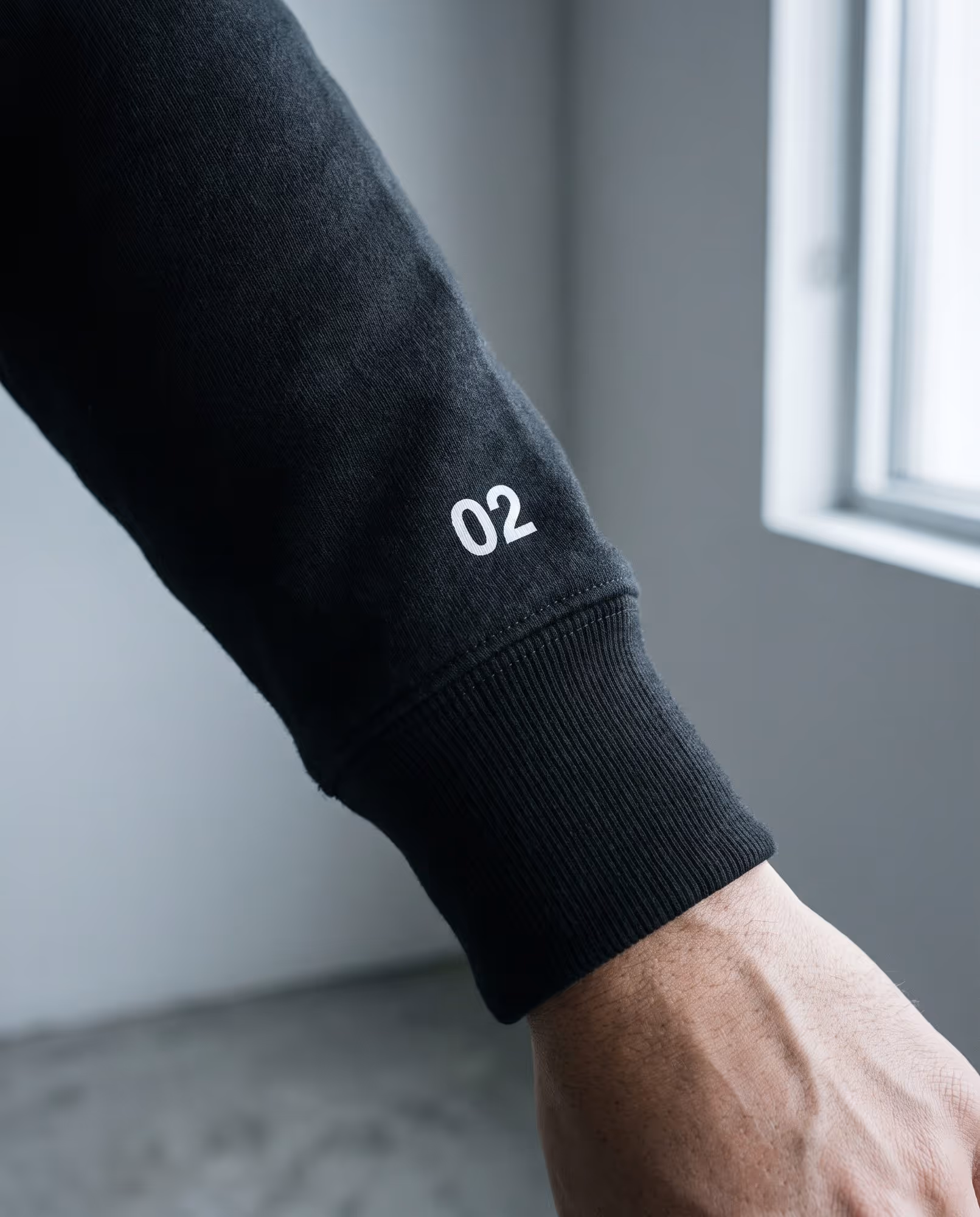 Close-up of a black crewneck cuff with a small printed number 02