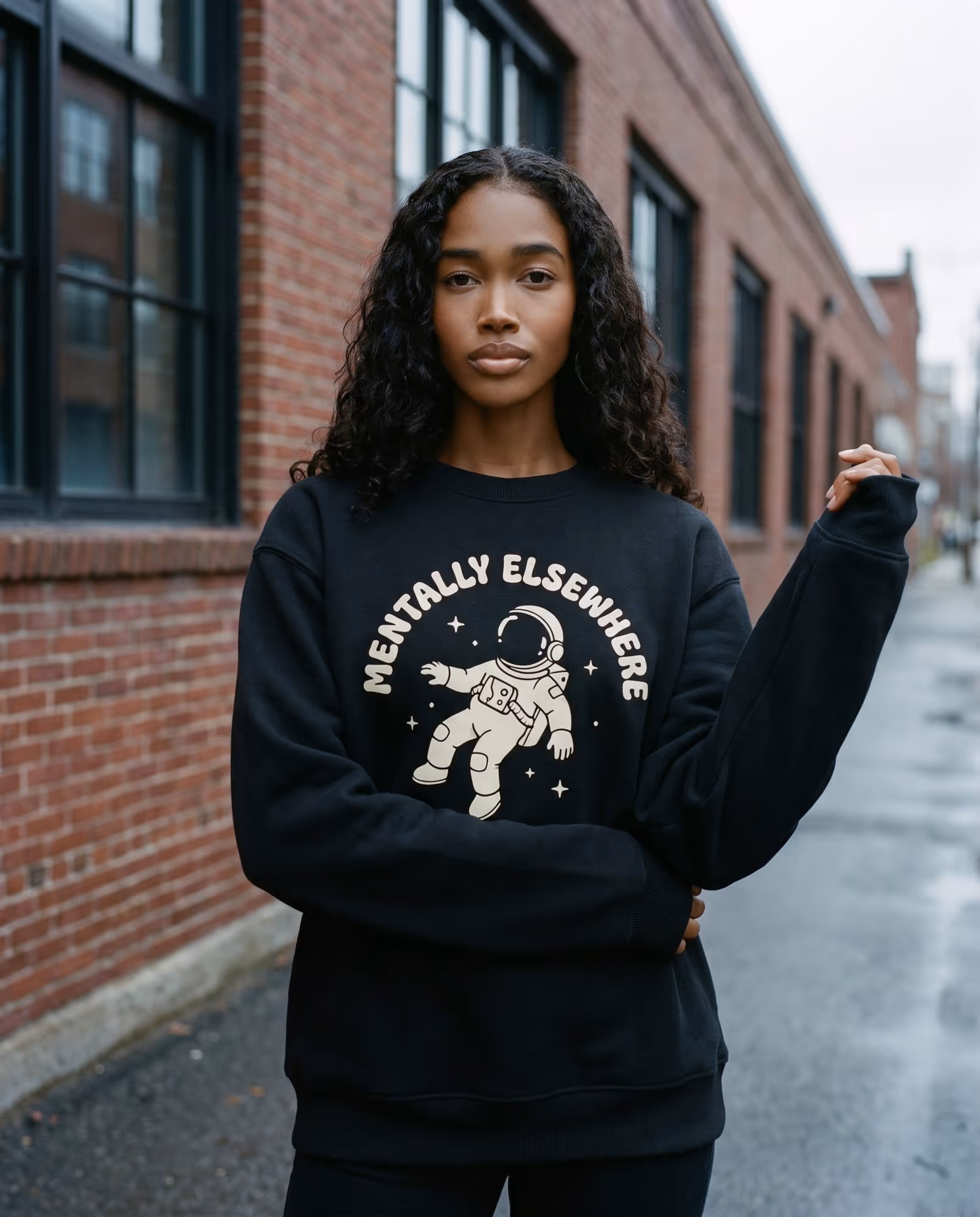 Model in a black crewneck fleece sweatshirt with a cream astronaut chest print, photographed on a Cambridge street