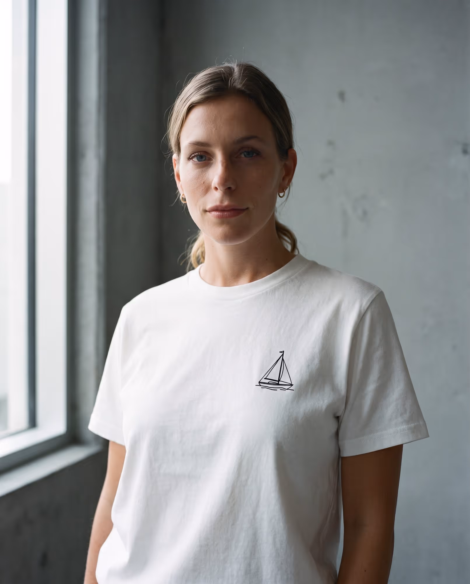 White t-shirt with a small black line-art sailing boat printed on the left chest