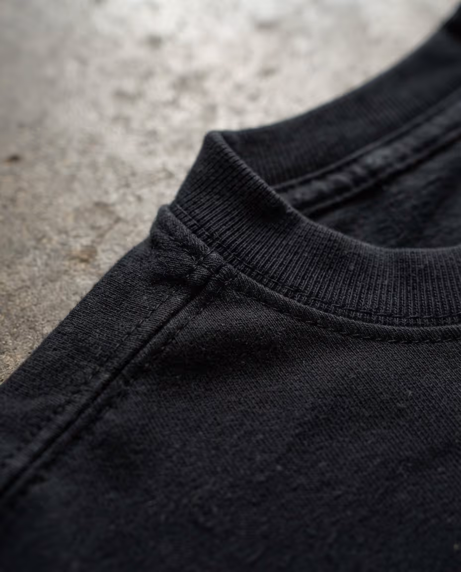 Close-up of the ribbed collar and shoulder seam on a black heavyweight cotton t-shirt