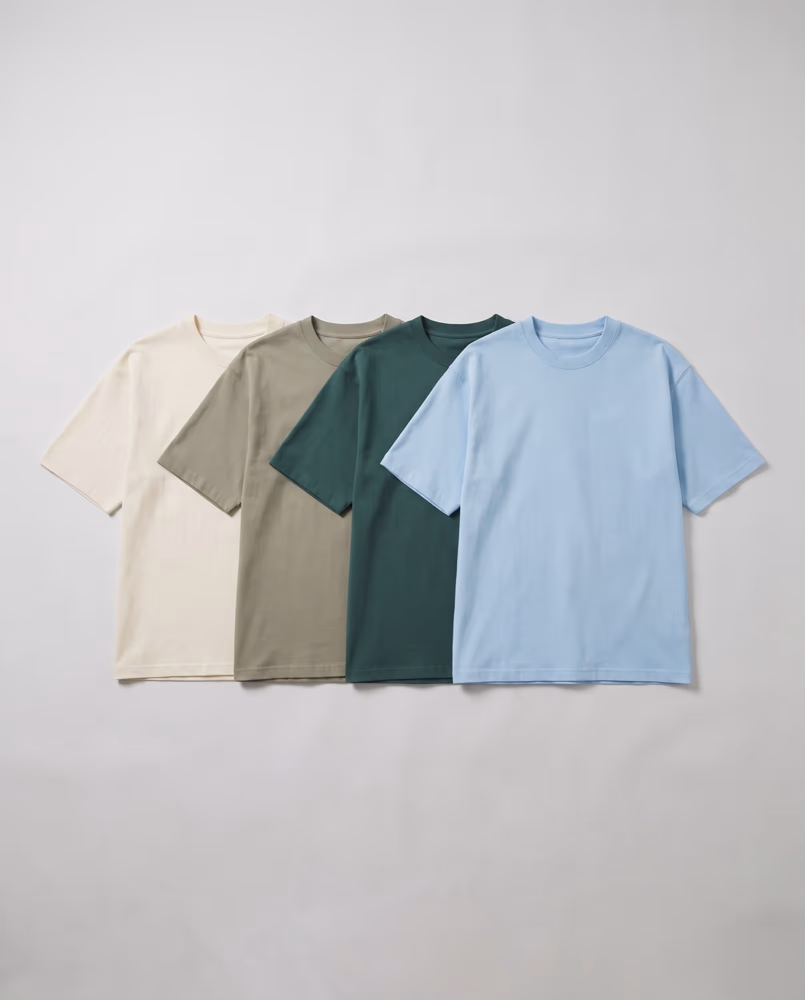 Cream, sage, pine green and sky blue oversized t-shirt blanks laid flat in a row