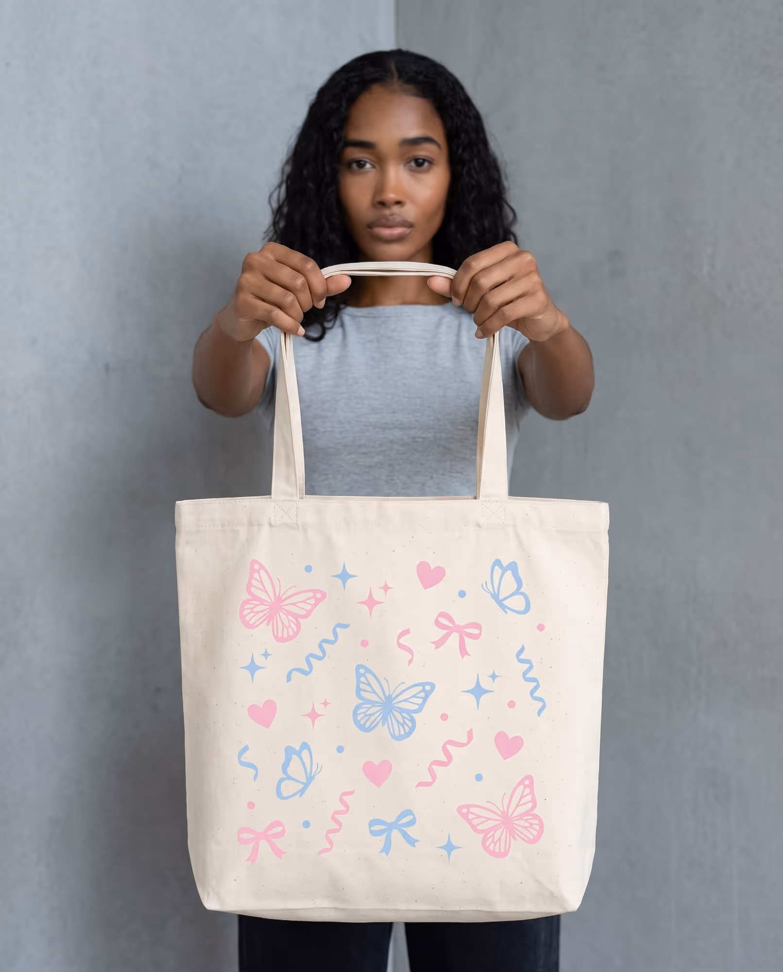 Natural canvas tote bag held up flat, printed with pink and pale blue butterflies, hearts, sparkles and bows
