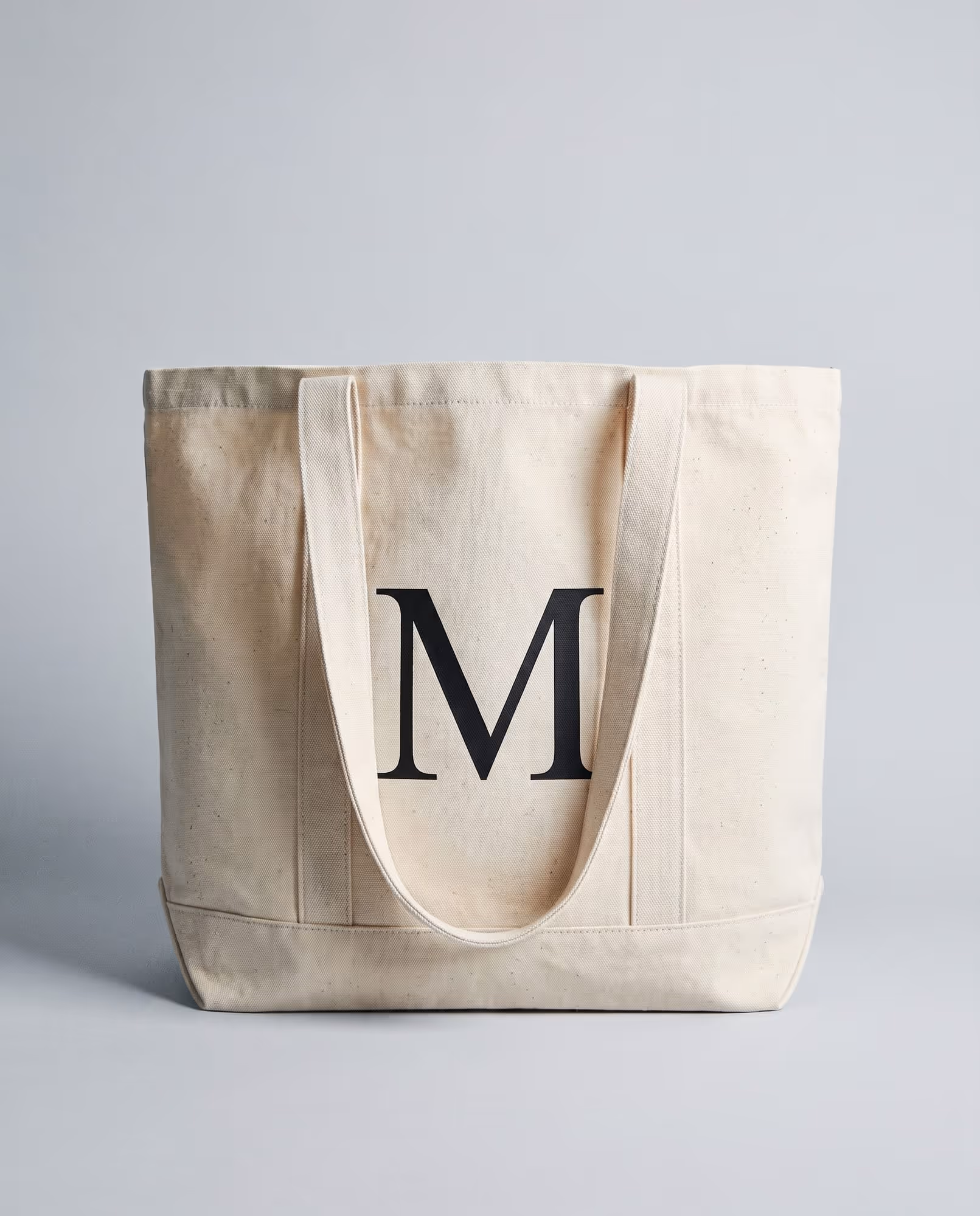 Natural canvas tote bag with a single large black serif letter M printed on the front