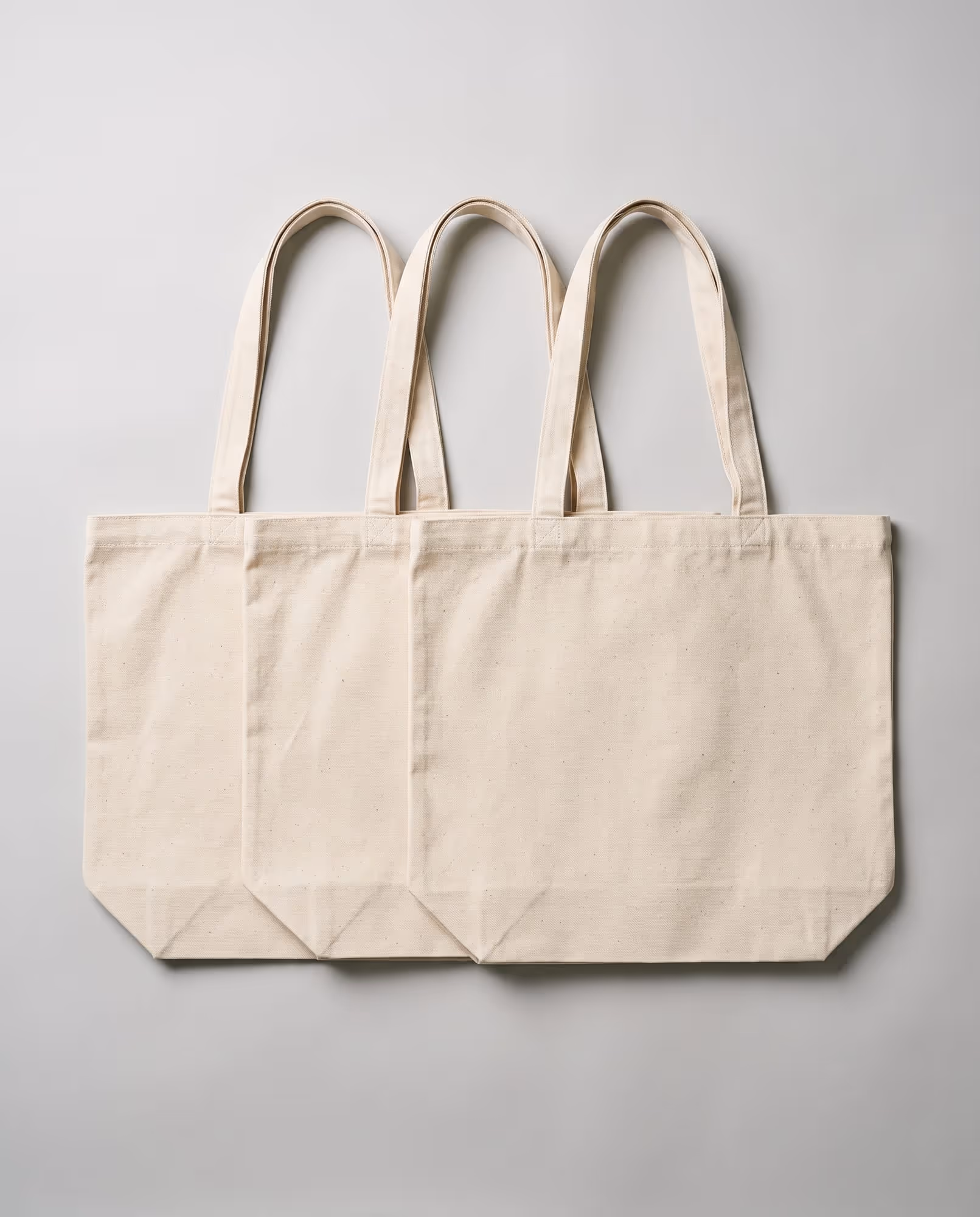 Three plain natural canvas tote bag blanks laid flat in a row